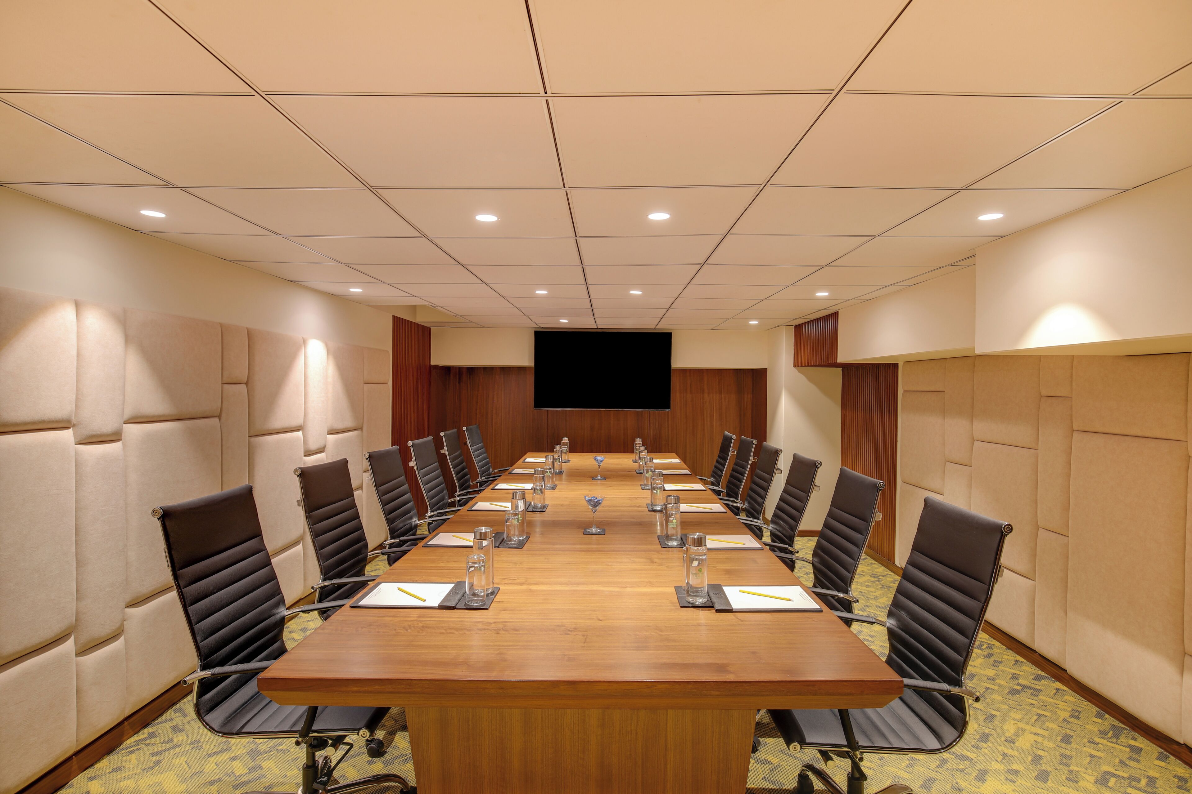 Un salón de conferencias con una mesa larga, sillas negras y un televisor de pantalla plana.