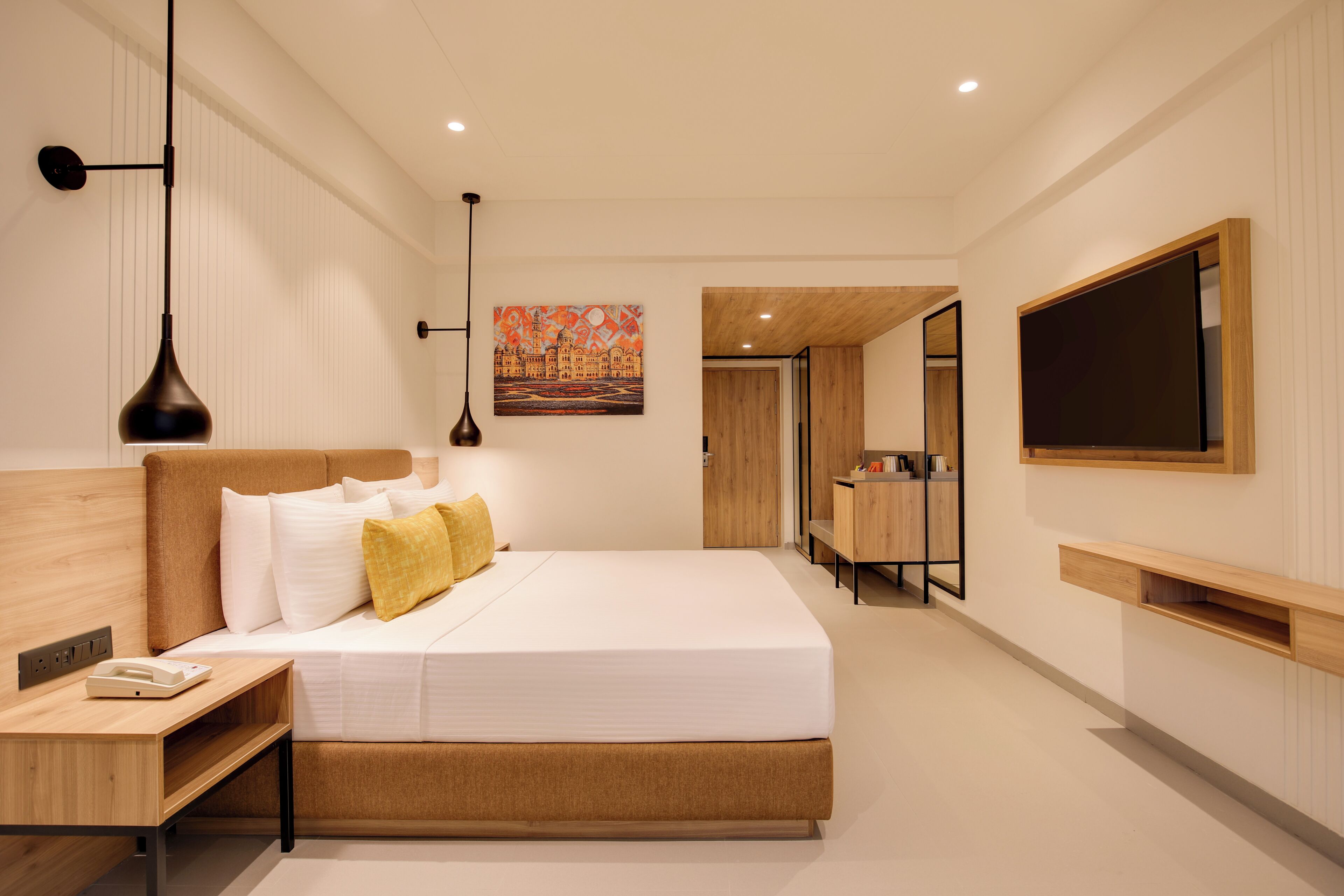 Una habitación de hotel moderna con una cama grande, mesitas de noche, un escritorio, un televisor y un cuadro en la pared.