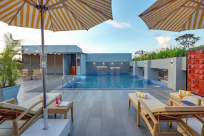 A pool area with lounge chairs and umbrellas, a stone wall, and a clear sky. - Lemon Tree Premier Vadodara (Vadodara)