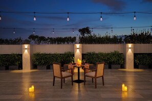 An outdoor dining area with a table and chairs, surrounded by plants and string lights. - Lemon Tree Premier Vadodara (Vadodara)