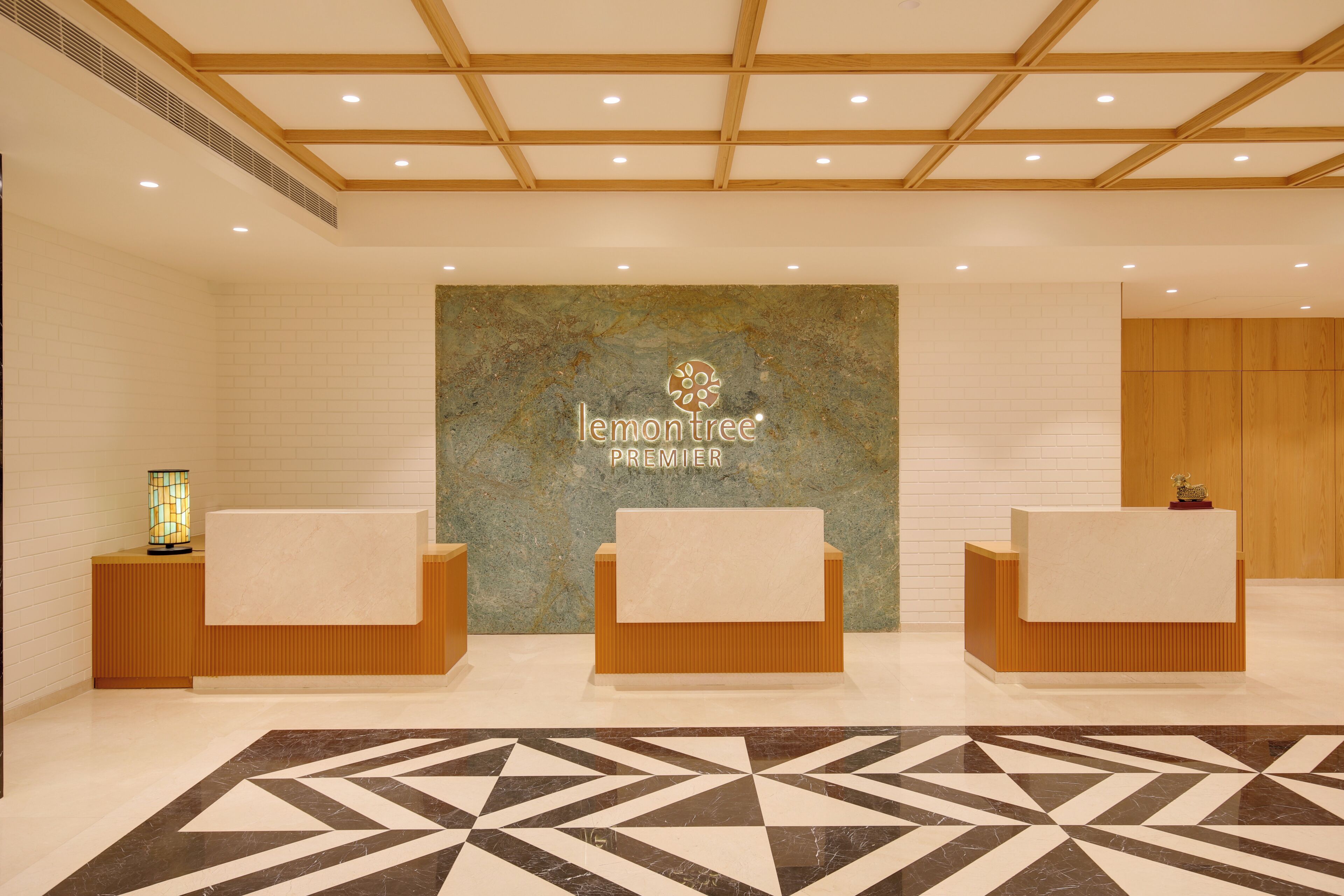 Un área de recepción con pared de mármol, tres mostradores de madera y un suelo con estampado geométrico.