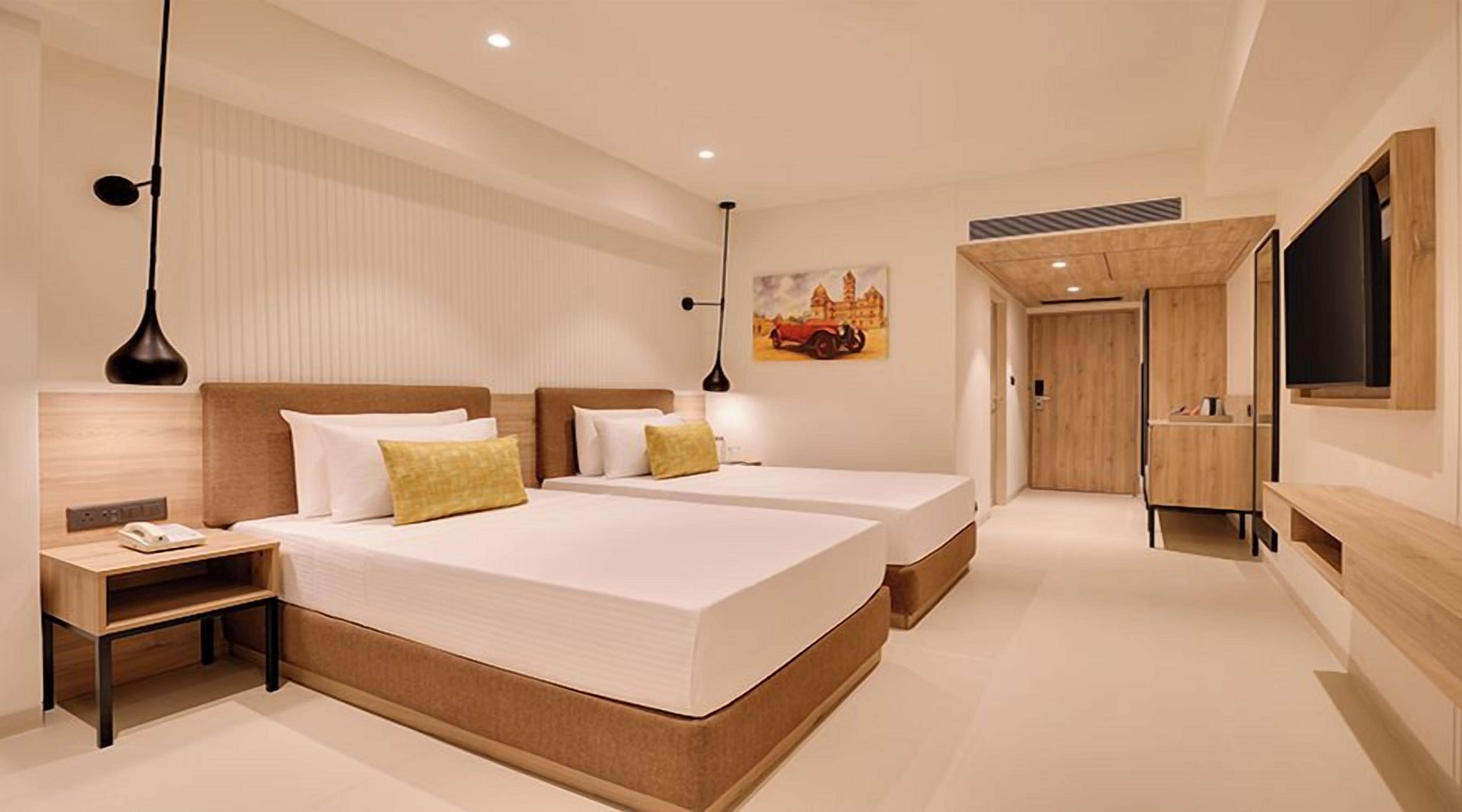 Habitación de hotel moderna con dos camas, cabecera de madera, mesita de noche, televisor de pantalla plana y un cuadro en la pared.