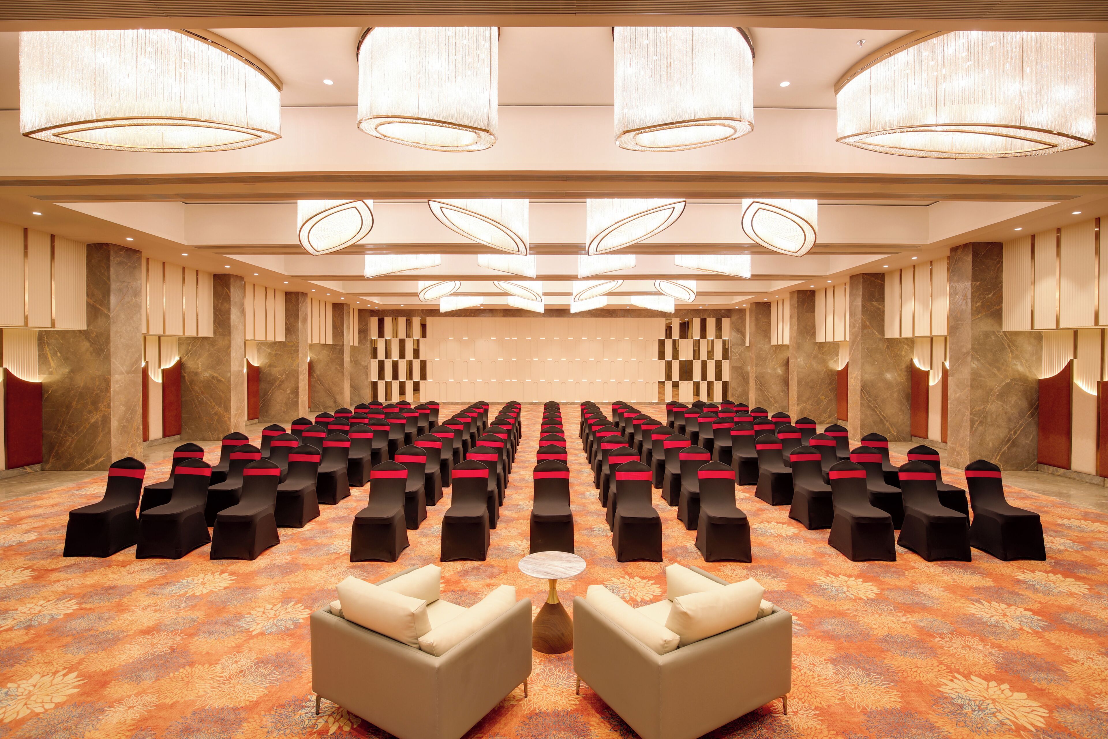 Un salón de conferencias con filas de sillas, un escenario y suelo alfombrado.