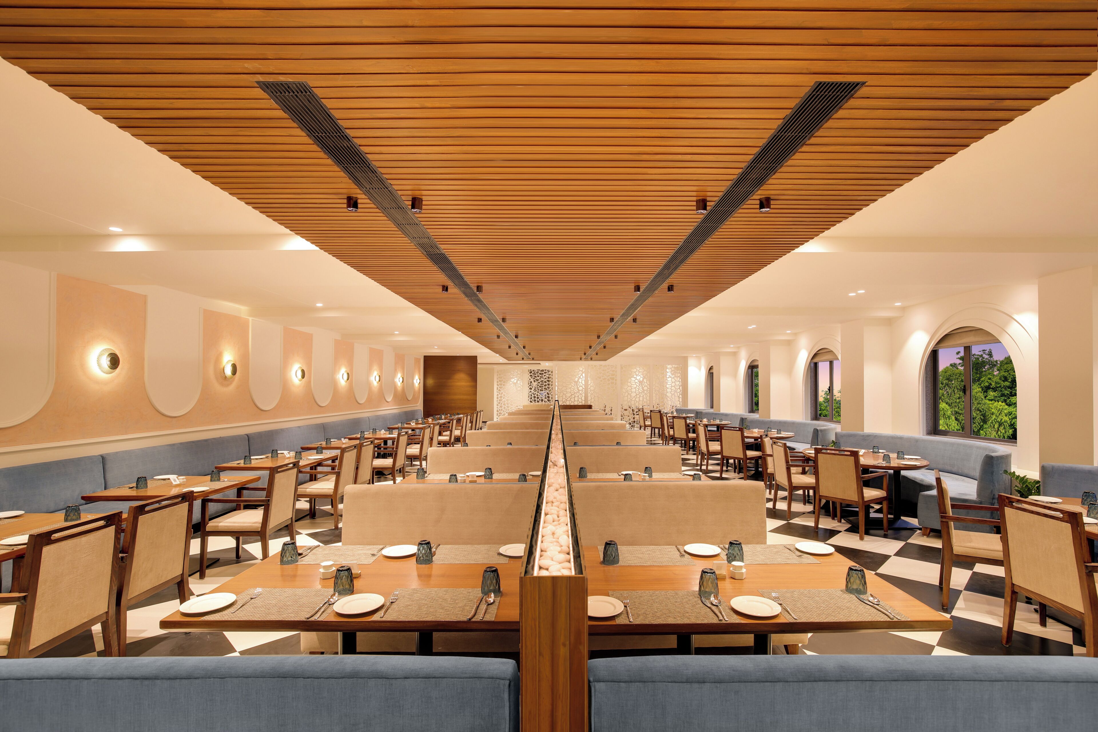A spacious dining area with multiple tables and booths, wooden ceiling, and natural light from windows.