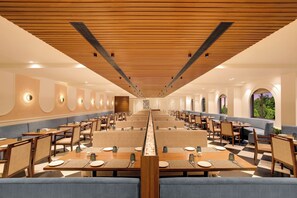 Un comedor amplio con varias mesas y cabinas, techo de madera y luz natural que entra por las ventanas.