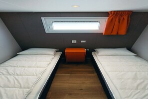 Ein kleiner, kompakter Raum mit zwei Betten, einem Fenster und Holzboden.
