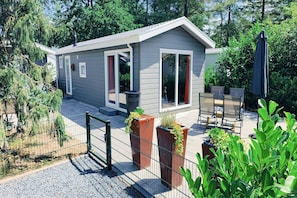 Ein kleines, eingeschossiges Haus mit überdachter Terrasse, einem eingezäunten Garten und verschiedenen Kübelpflanzen.