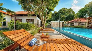 Un espace aménagé au bord de la piscine, avec des chaises longues en bois, une piscine et un bâtiment portant l’inscription « AURORA ».
