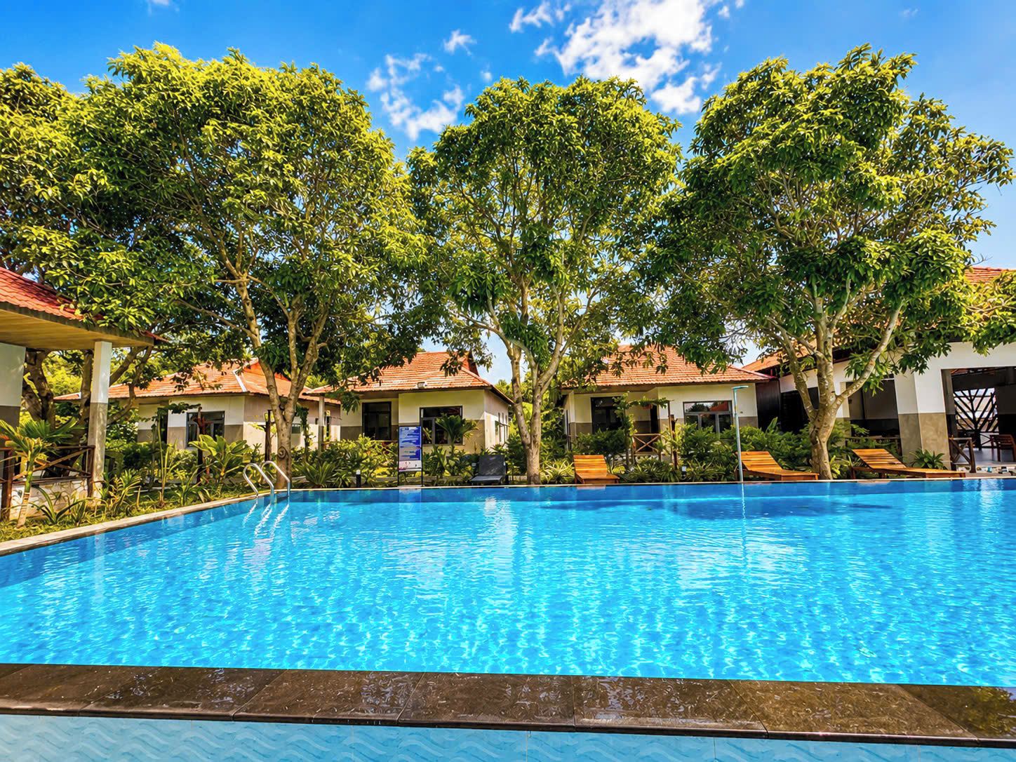 A swimming pool surrounded by trees and buildings with red-tiled roofs.