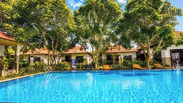 A swimming pool surrounded by trees and buildings with red-tiled roofs.