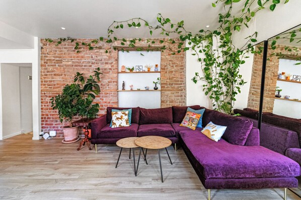 A living room with a brick wall, a purple sofa, a coffee table, and a large potted plant.
