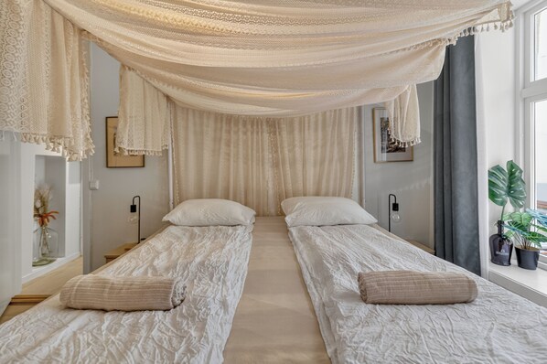 A room with two beds, a large window, and a plant.