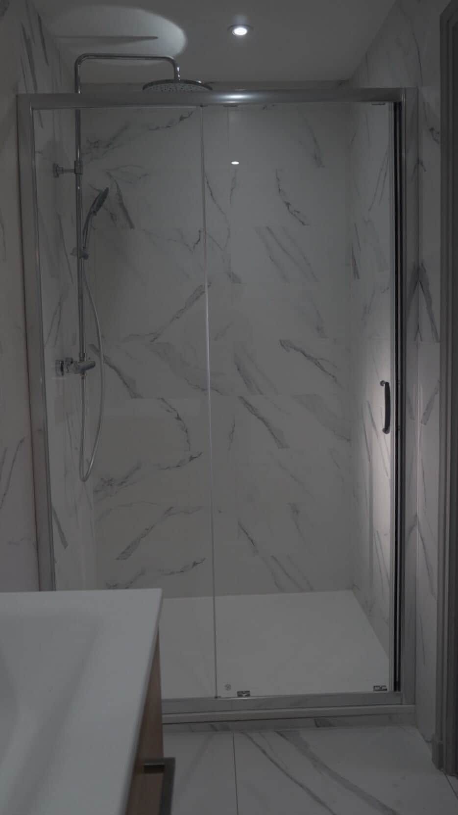 Een badkamer met een glazen douchecabine, een witte marmeren wand en een houten vloer.