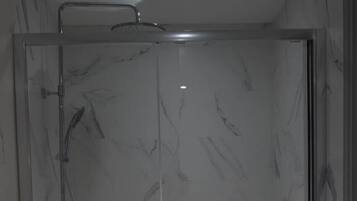 Een badkamer met een glazen douchecabine, een witte marmeren wand en een houten vloer.