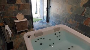 A bathroom with a large bathtub, a towel rack, and a small cabinet. - Jacoumard's Interlude* Private Jacuzzi* Air Conditioning (Domme)