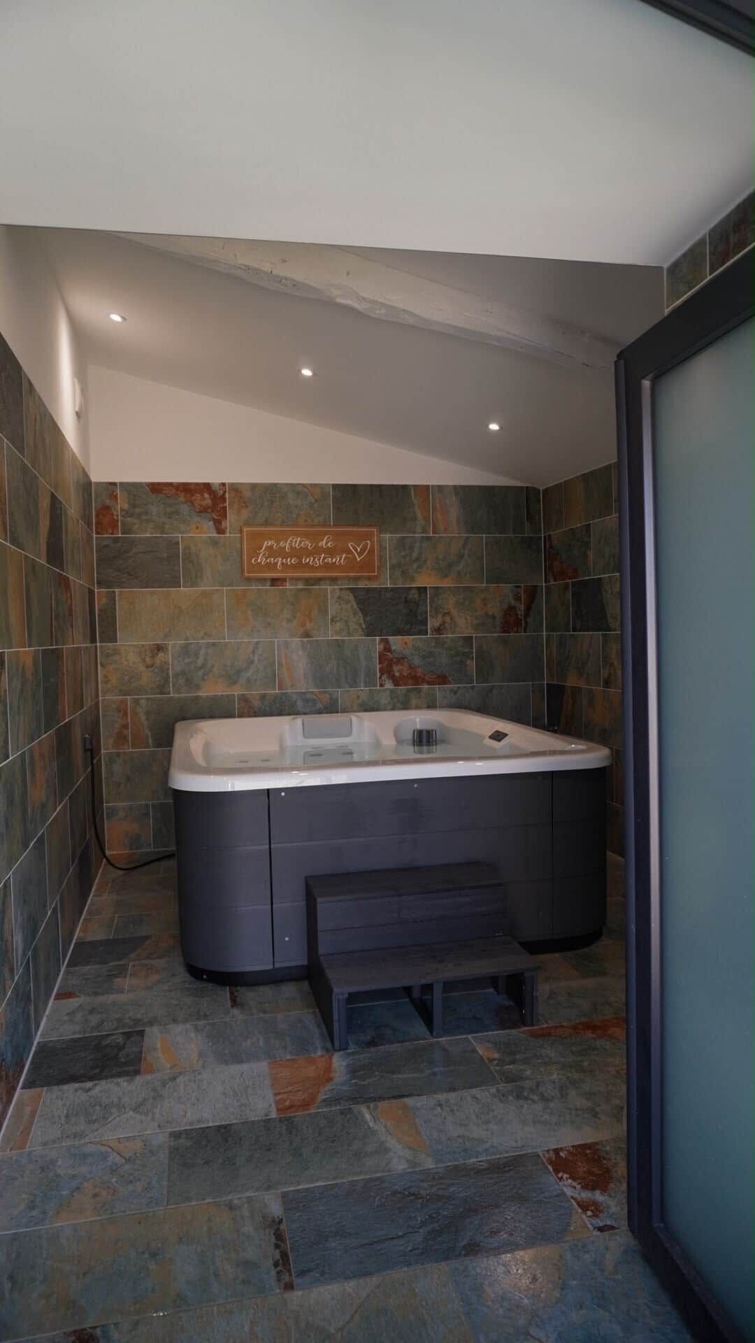 Une salle de bain moderne avec une baignoire îlot, des carreaux de pierre aux murs et sur le sol, et un banc placé devant la baignoire.