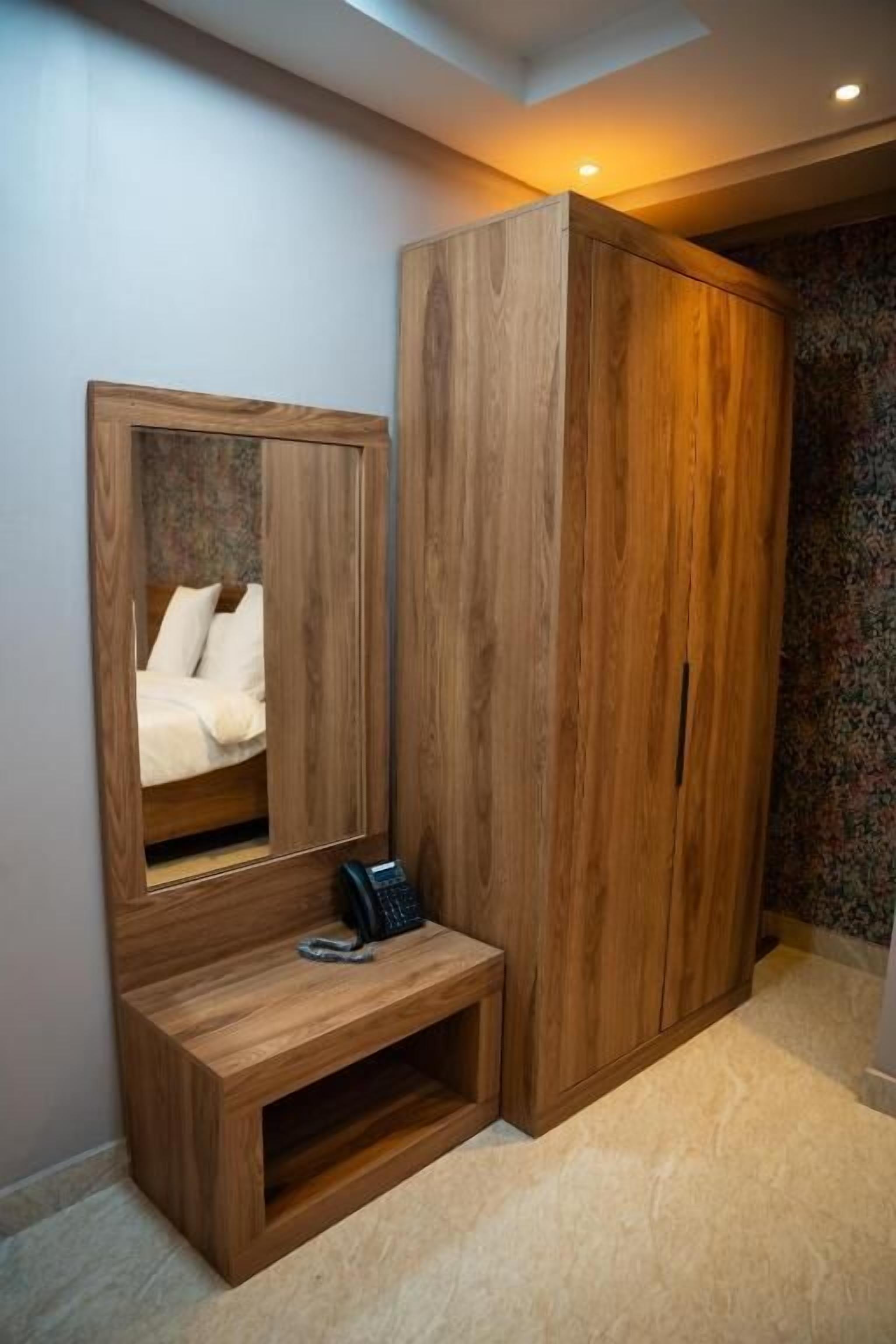 A wooden wardrobe with a mirror, a small bench, and a telephone.