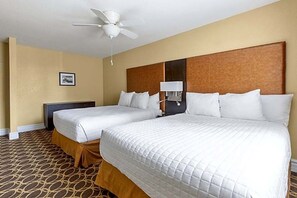 Ein Hotelzimmer mit zwei Queensize-Betten, einem Deckenventilator, einem Nachttisch und einer an der Wand befestigten Lampe.