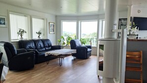 En stue med en sort lædersofa, en blå lænestol og et lille bord. Der er et hvidt køleskab og en træstol i hjørnet.