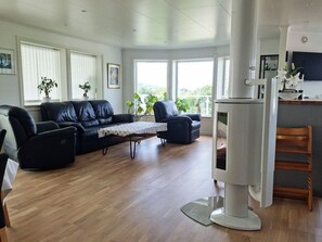 Ein Wohnzimmer mit einem schwarzen Ledersofa, einem blauen Sessel und einem kleinen Tisch. In der Ecke steht ein weißer Kühlschrank und ein hölzerner Stuhl.