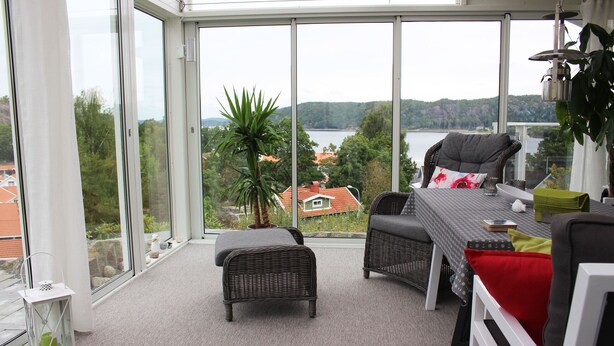 En balkon med fletningsmøbler, udsigt over et sø og et hus i det fjerne.