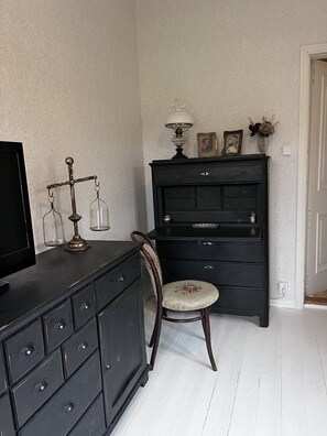 Ein Zimmer mit einem schwarzen Kommode, einem Stuhl, einem Fernseher und einer Wand mit strukturiertem Wandpapier.