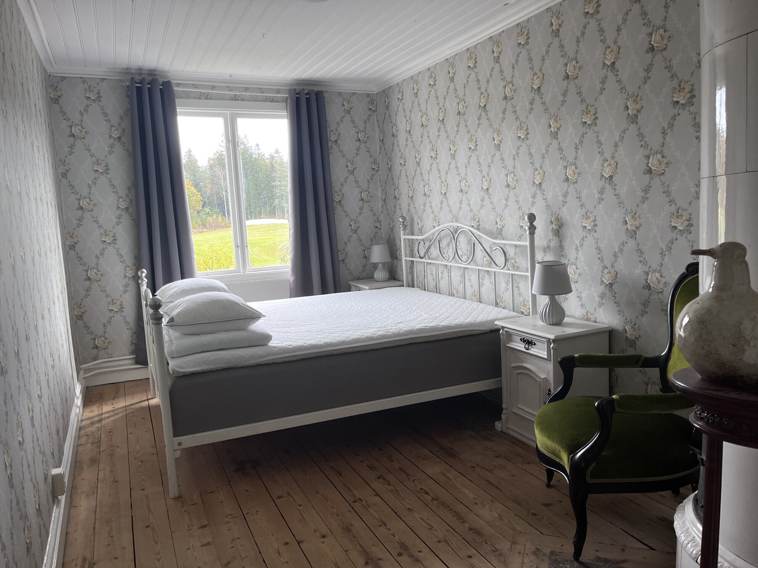 Une chambre à coucher avec un lit, une table de chevet, une chaise et une fenêtre avec des rideaux.