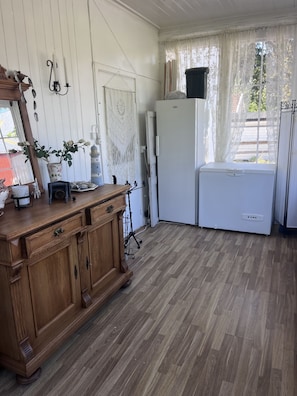 Ein Zimmer mit einem Holzschrank, einem weißen Kühlschrank und einem Fenster mit Spitzenvorhängen.