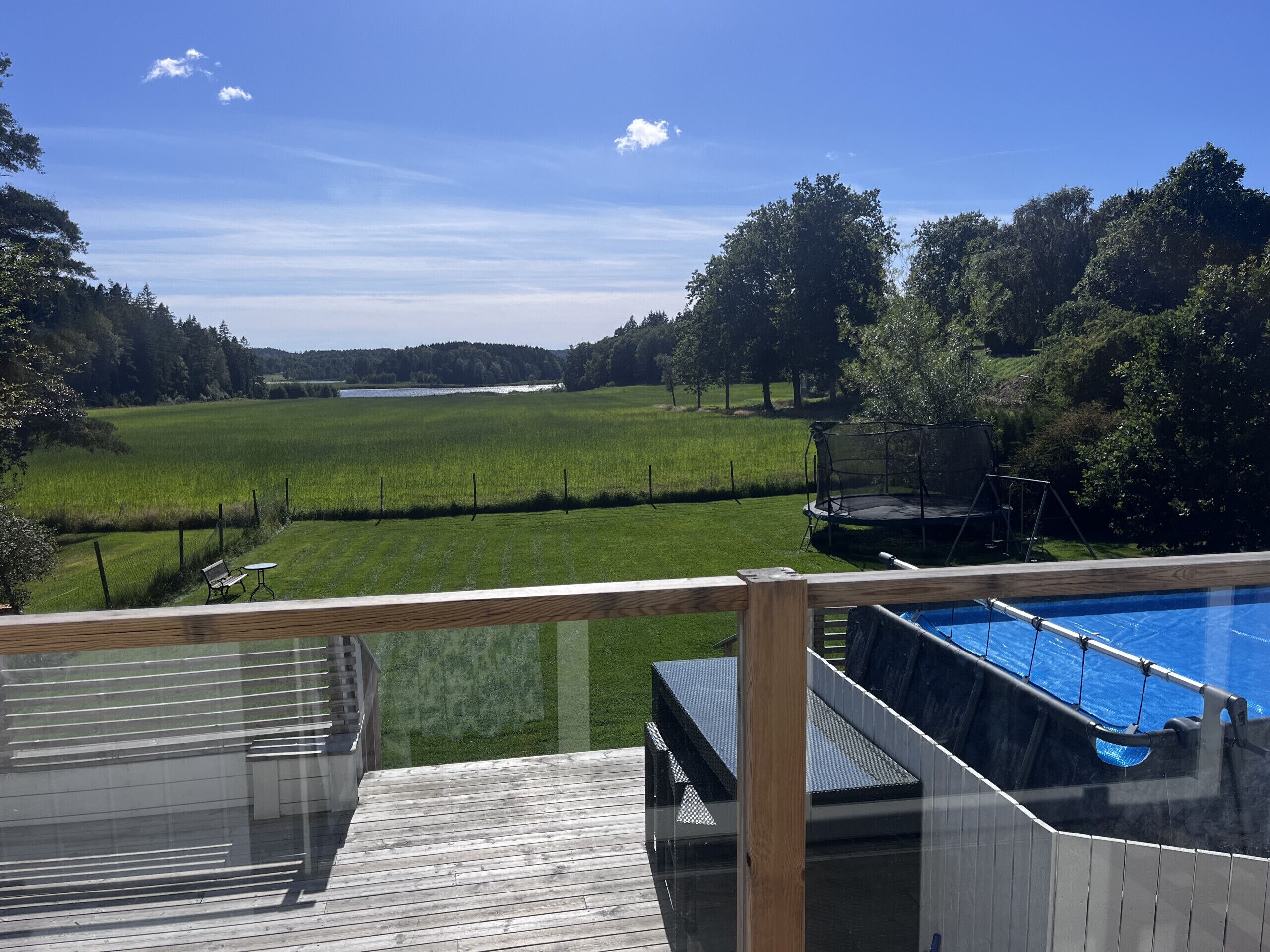 Une piscine dotée d’une terrasse en bois et offrant une vue sur un champ verdoyant et des arbres.