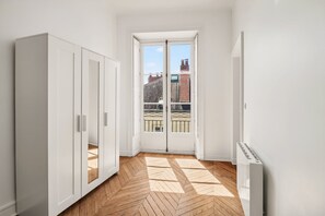 A narrow room with a wooden herringbone floor, white walls, and a door leading to a balcony with a view of buildings. - 90 m² of charm and comfort in the heart of Nantes (Nantes)