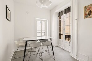 Ein kleiner, heller Raum mit einem weißen Tisch und Stühlen, einem Fenster mit Rollläden und einer zur Außenseite führenden Tür.