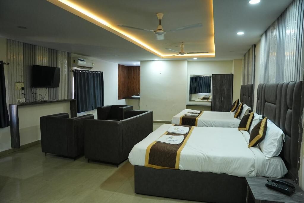 Habitación de hotel con una cama grande, dos mesitas de noche, televisor de pantalla plana, ventilador de techo y una zona de estar con sofá y sillones.