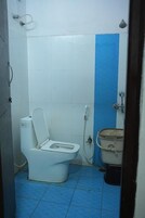 Ein kleines Badezimmer mit Toilette, blauer Wand und einem Metalleimer.