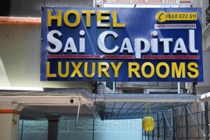 Señal que dice 'HOTEL Sai Capital HABITACIONES DE LUJO' con números de contacto y un número GSTIN.
