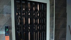 Un ascenseur moderne doté d’une porte métallique aux motifs géométriques, installé devant un mur de pierre et muni d’un écran numérique affichant le chiffre 3.