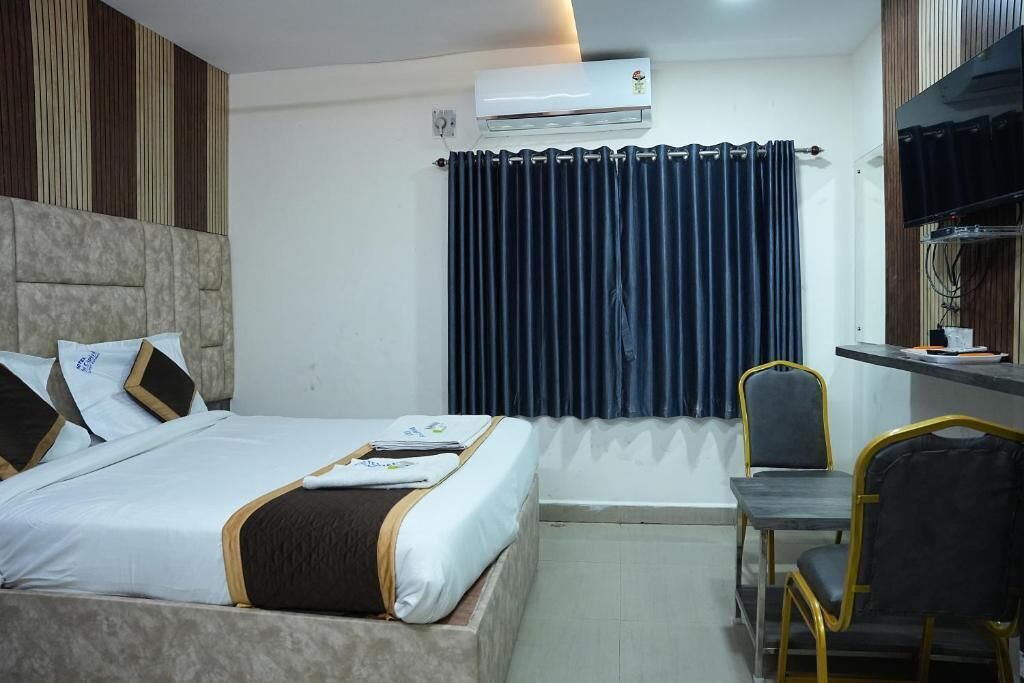 A hotel room with a bed, a desk, a chair, an air conditioning unit, and a television.