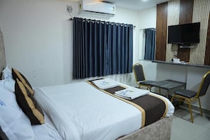 Una habitación de hotel con una cama, un escritorio, una silla, un televisor y aire acondicionado.