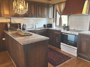 A kitchen with dark wood cabinets, a granite countertop, a built-in oven, and a chandelier. - Dream home by the golf course in Åtvidaberg |SE10025 (Åtvidaberg)
