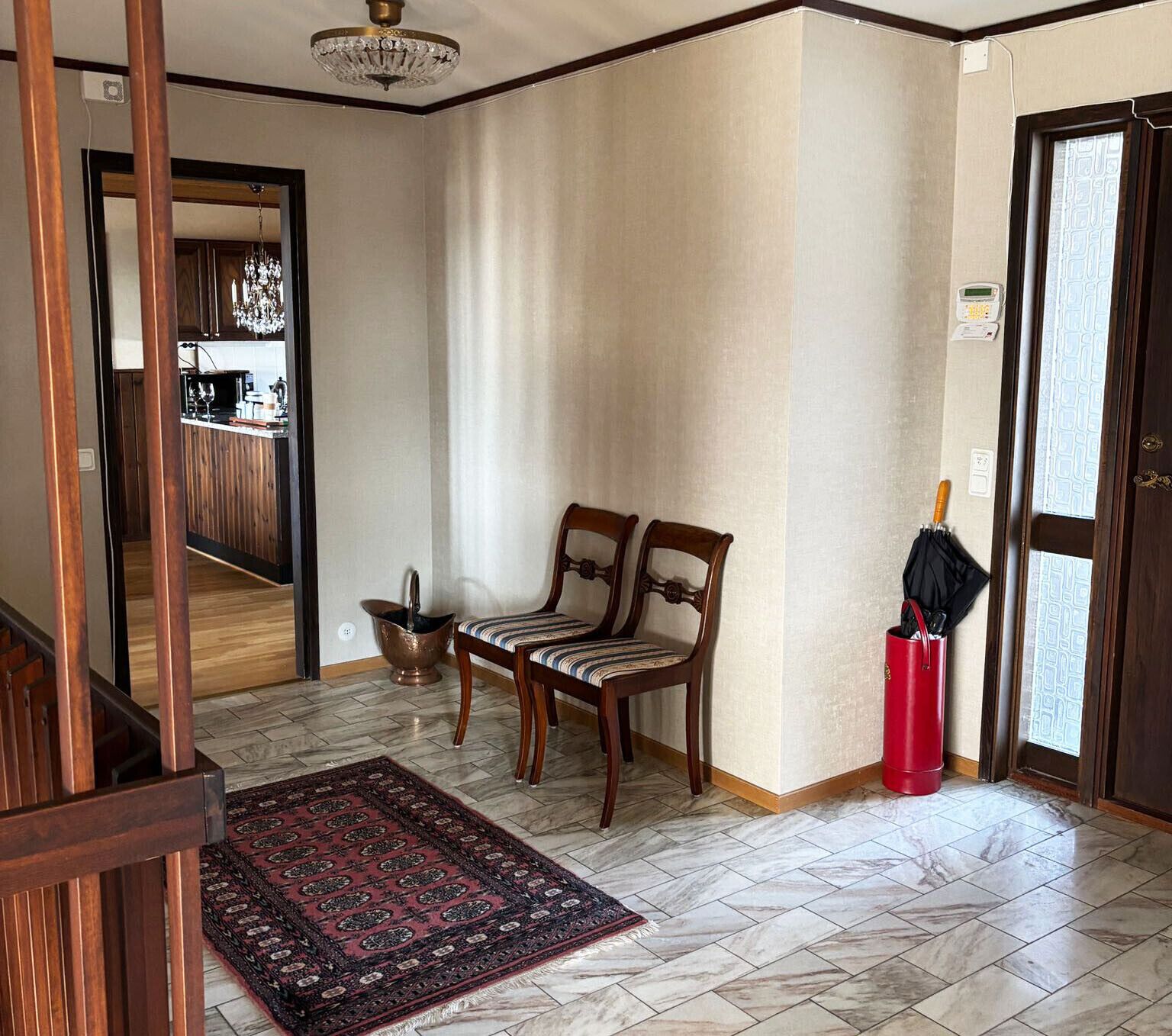 Une pièce comprenant une chaise en bois, une petite table, une poubelle rouge et un tapis à motifs.