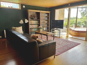 A living room with a leather sofa, a bookshelf, a television, and a large window with a view of greenery. - Dream home by the golf course in Åtvidaberg |SE10025 (Åtvidaberg)