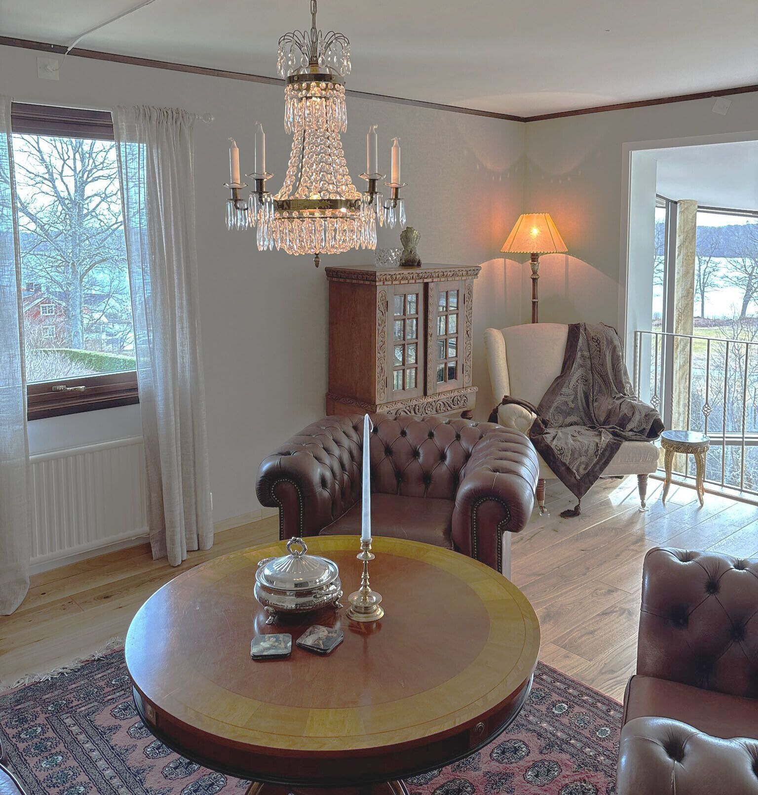 A living room with a chandelier, a fireplace, a sofa, a lamp, and a view through the window.