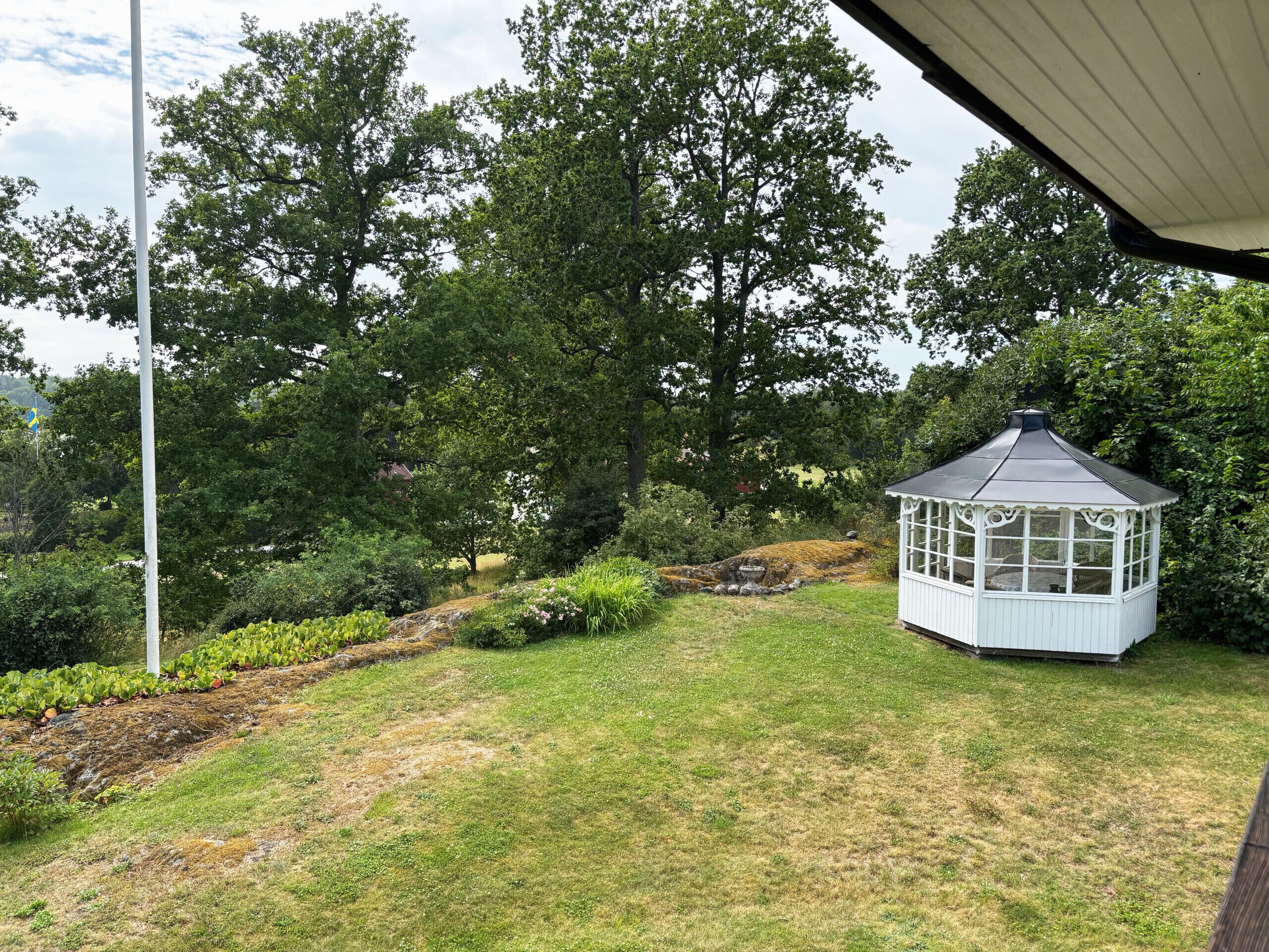 A gazebo with a glass roof, surrounded by a grassy area and trees.