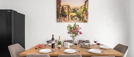 A dining room with a long table set for six, a black refrigerator, and a painting of a landscape on the wall.