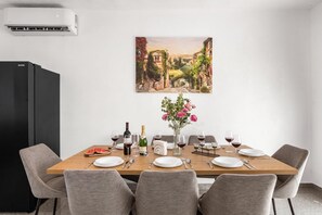 Ein Esszimmer mit einem langen Tisch, gedeckt für sechs Personen, einem schwarzen Kühlschrank und einem Landschaftsbild an der Wand.
