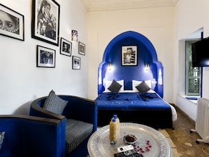 A room with a bed, a sofa, a coffee table with a bottle and remote, and framed pictures on the wall. - Palais Laya (Marrakesh)