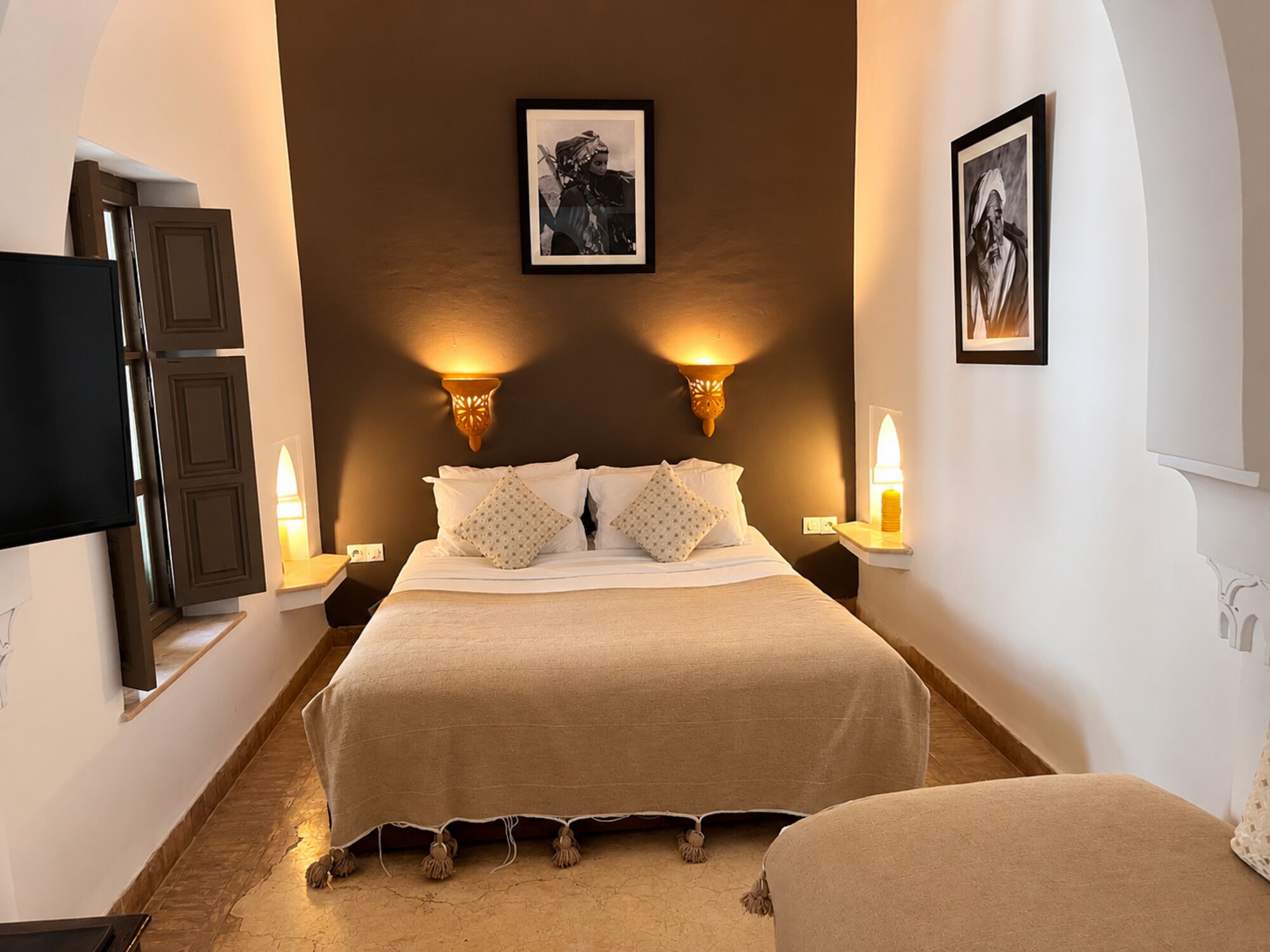 A bedroom with a large bed, two wall-mounted lamps, a flat-screen TV, and two framed pictures on the wall.