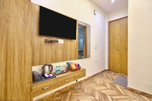 A hotel room with a flat-screen TV mounted on the wall, a wooden wardrobe, a small kitchenette with a kettle, and a herringbone-patterned floor. - The Rosewalk Vista By Mannat (New Delhi)