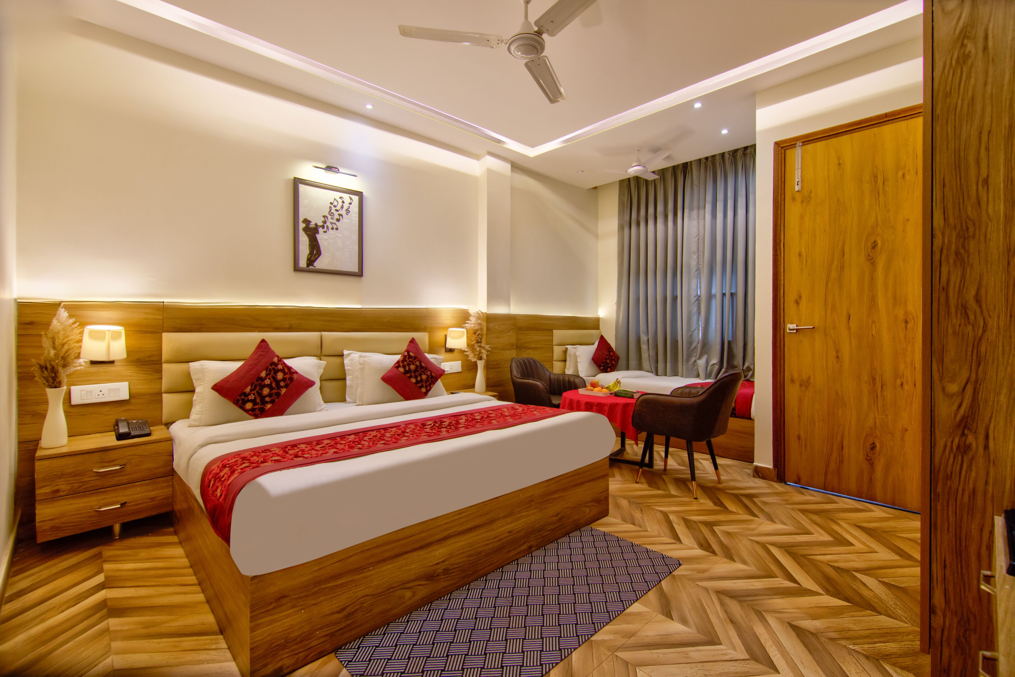Quarto de hotel com uma cama grande, mesas de cabeceira, escrivaninha, cadeira, guarda-roupa e ventoinha no teto.