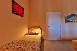 A small, single-bed room with a door and a painting on the wall. - Beachfront Sunset Apartments Sutomore - Studio Apartment with Sea View and Terrace (Sutomore)