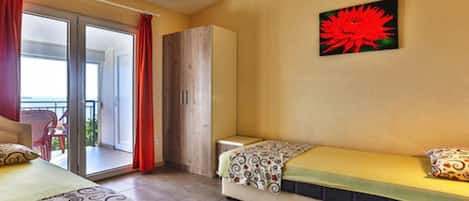 A hotel room with two beds, a wardrobe, a balcony with red curtains, and a painting on the wall.